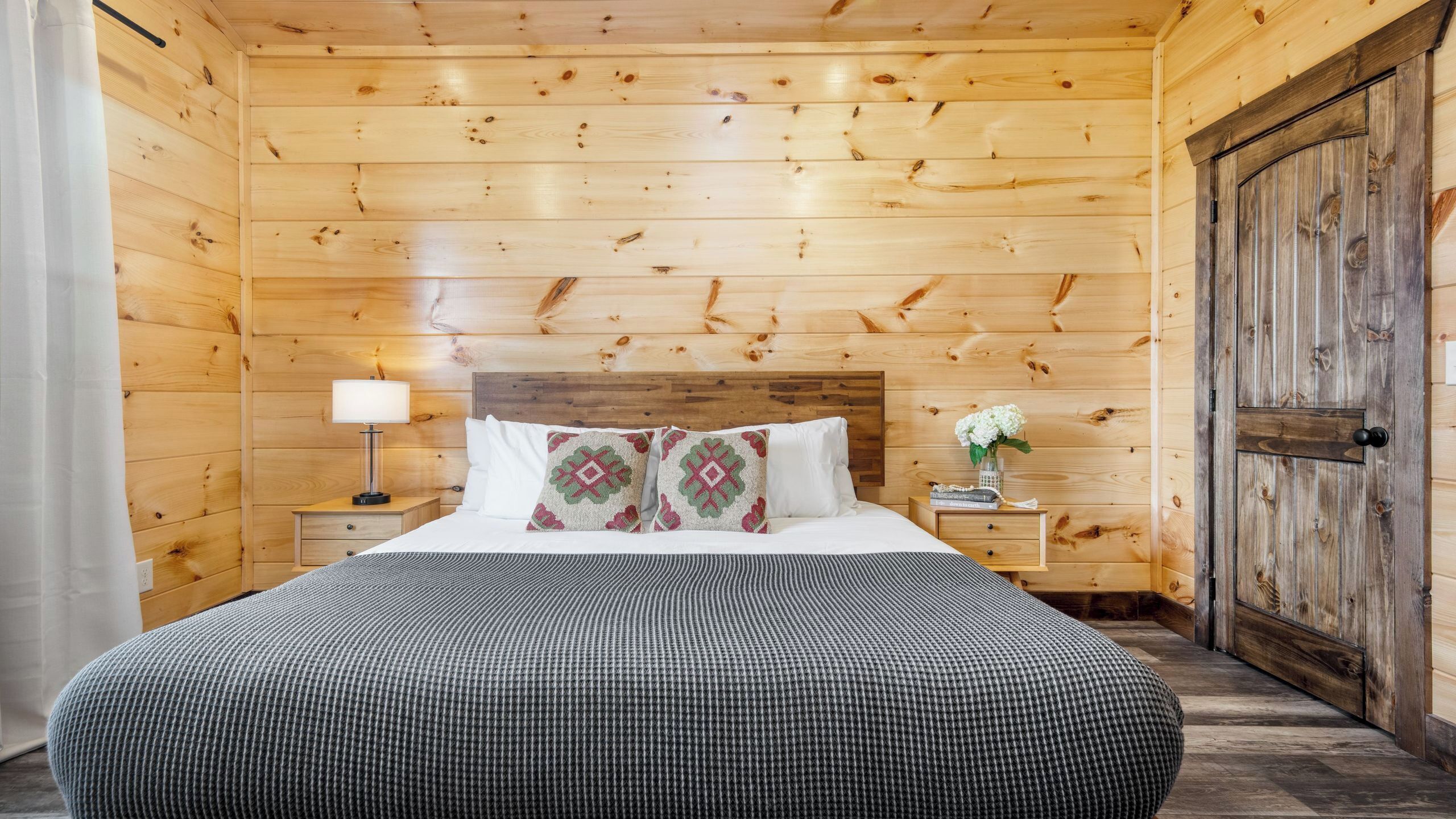 A wooden-paneled room with a bed, a nightstand, a lamp, and a door.