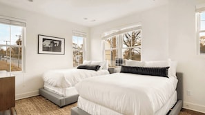 A bedroom with two beds, a gray sofa, a framed picture, and large windows.