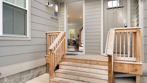 A wooden staircase leading to a house entrance with a porch, a mailbox, and a door with a number plate.
