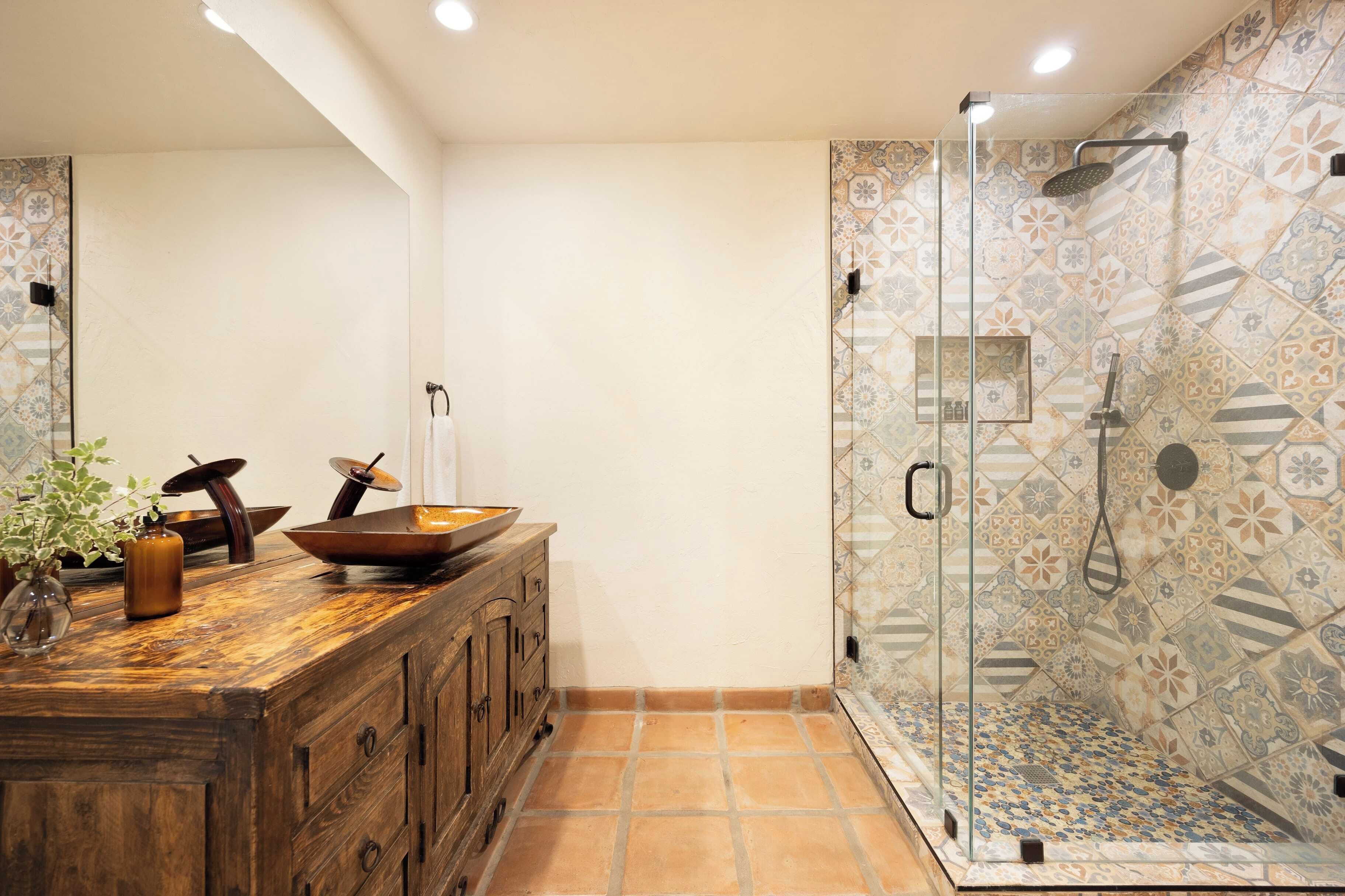 A bathroom with a wooden vanity, a glass shower enclosure, and patterned tile walls.