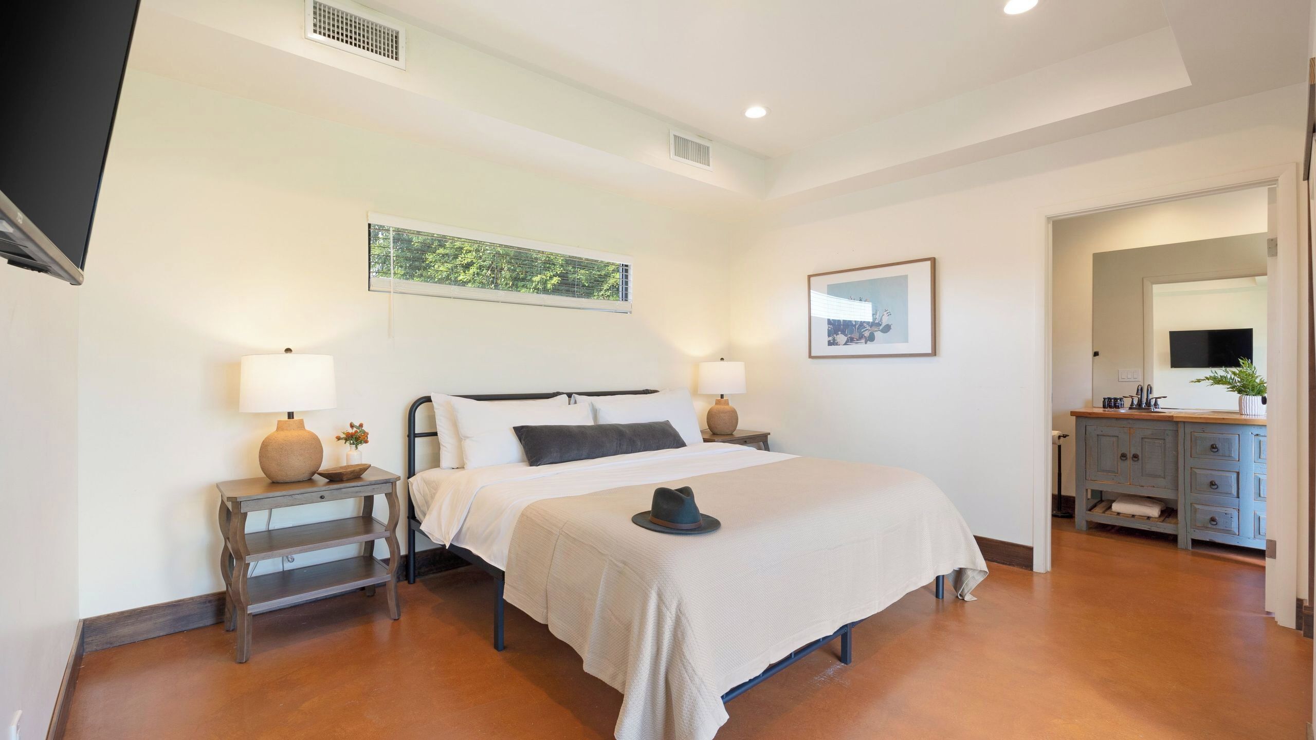 A bedroom with a bed, bedside tables, lamps, a picture on the wall, a mirror, and a dresser.