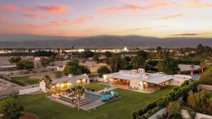 A modern resort with multiple buildings, a swimming pool, and a view of distant mountains. - Sleeps 20! Architectural Mansion w/ Pool, Indoor Tennis Court, Game Room Starlight Estate by Avantstay (Indio)