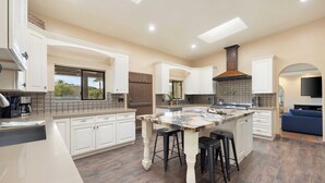 A spacious kitchen with a large island, white cabinetry, and a modern design. - Sleeps 20! Architectural Mansion w/ Pool, Indoor Tennis Court, Game Room Starlight Estate by Avantstay (Indio)