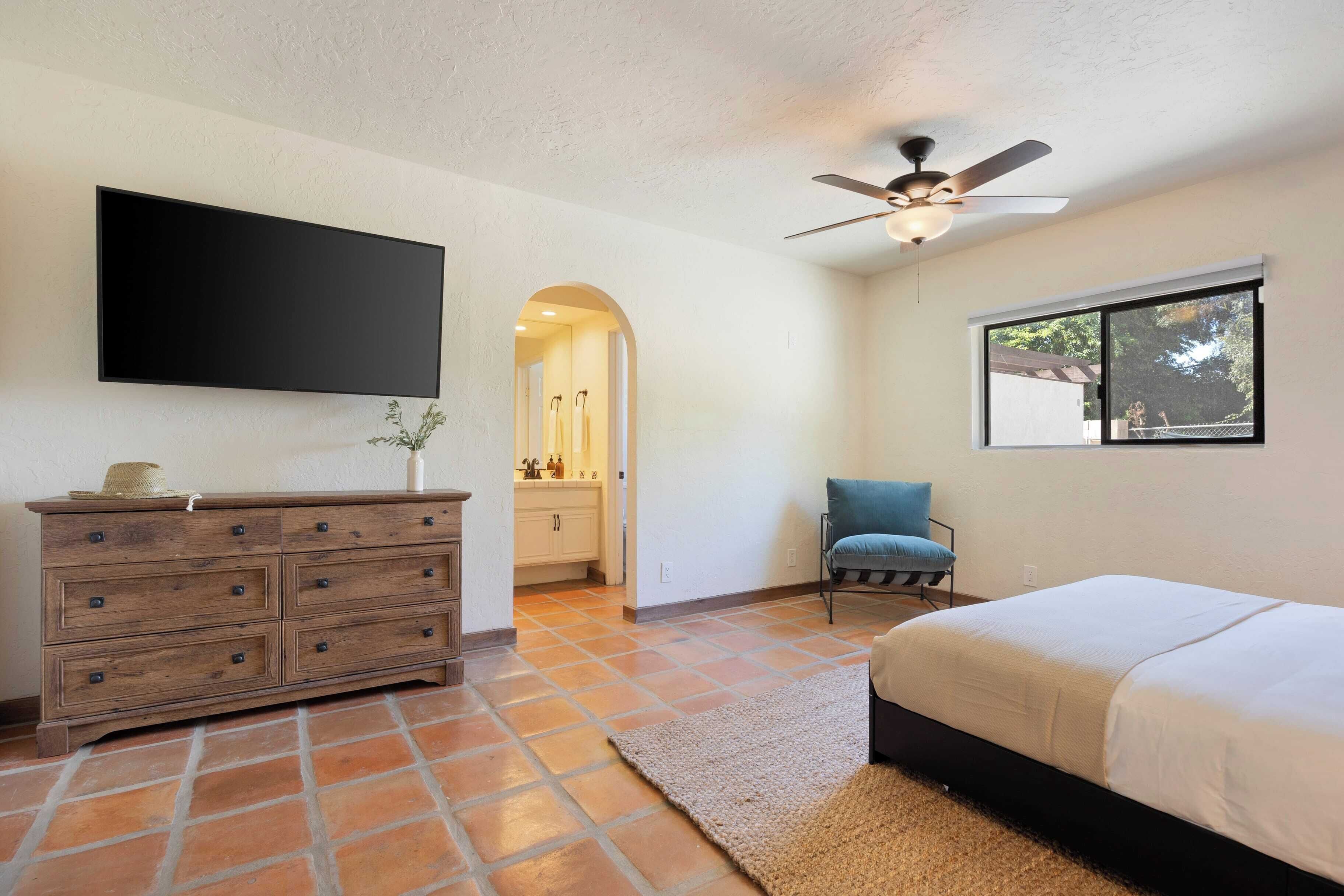 A bedroom with a bed, a dresser, a chair, a TV, and a ceiling fan.