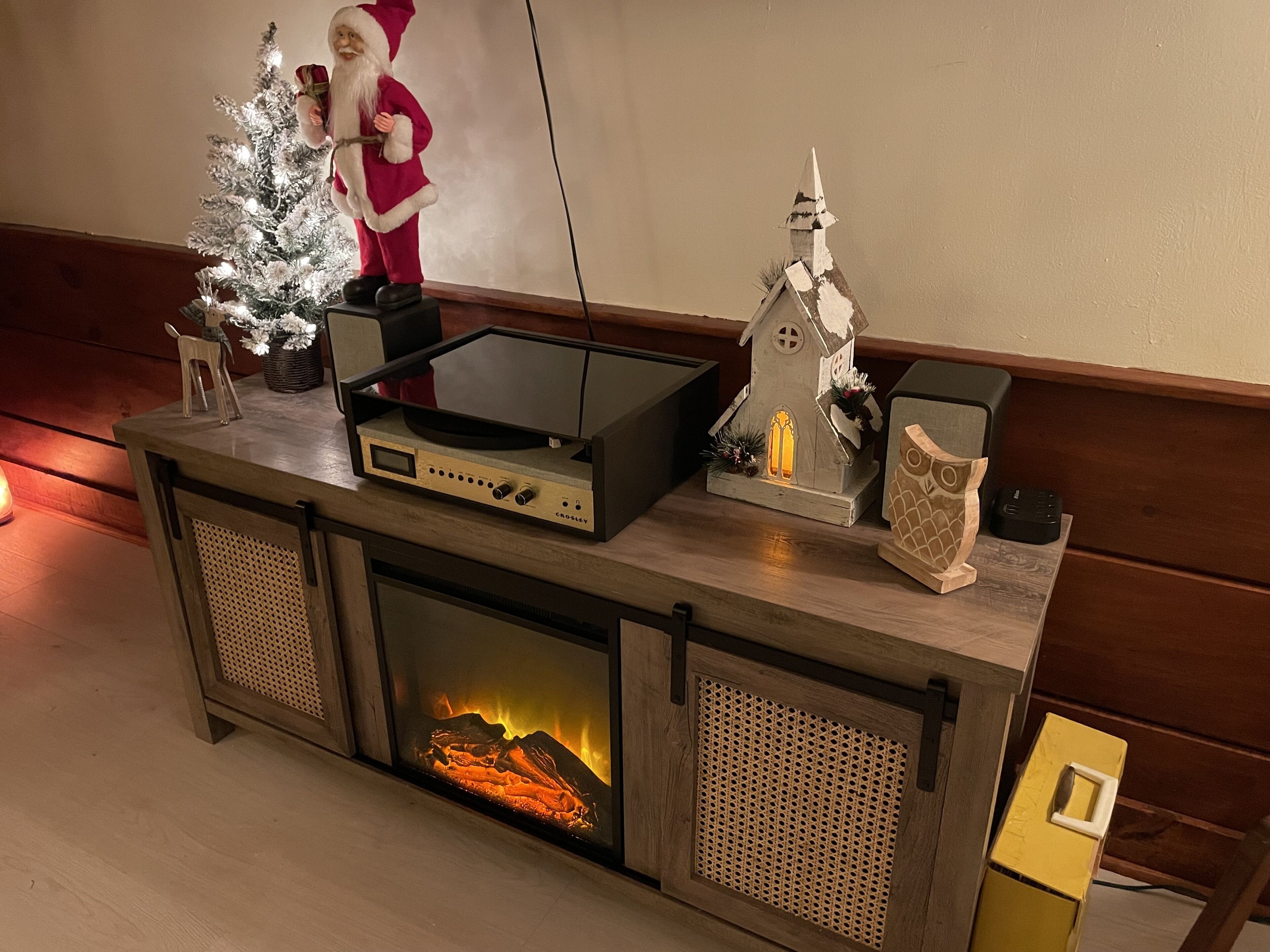 A wooden entertainment center with a flat-screen TV, a fireplace, and holiday decorations.