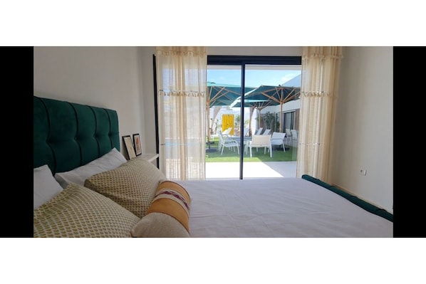A bedroom with a large bed, a view of the outdoor area, and a sliding glass door.