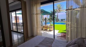 A bedroom with a large window overlooking a pool and garden.