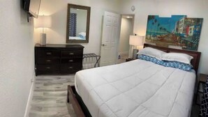 Ein Schlafzimmer mit Bett, Schminktisch, Spiegel, Tür und einem Bild an der Wand.