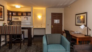 A compact hotel room with a kitchenette, a dining area with a table and chairs, a sofa, a desk with a lamp, and a framed picture on the wall. - Mountain View Studio + Pool Access (Colorado Springs)