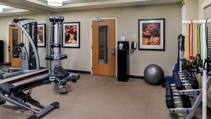 Een fitnessruimte met trainingsapparatuur, een spiegel, een deur en een muur met ingelijste foto's.