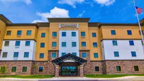Et flere-etagers Staybridge Suites hotel med en stenfacade, mange vinduer og det amerikanske flag.