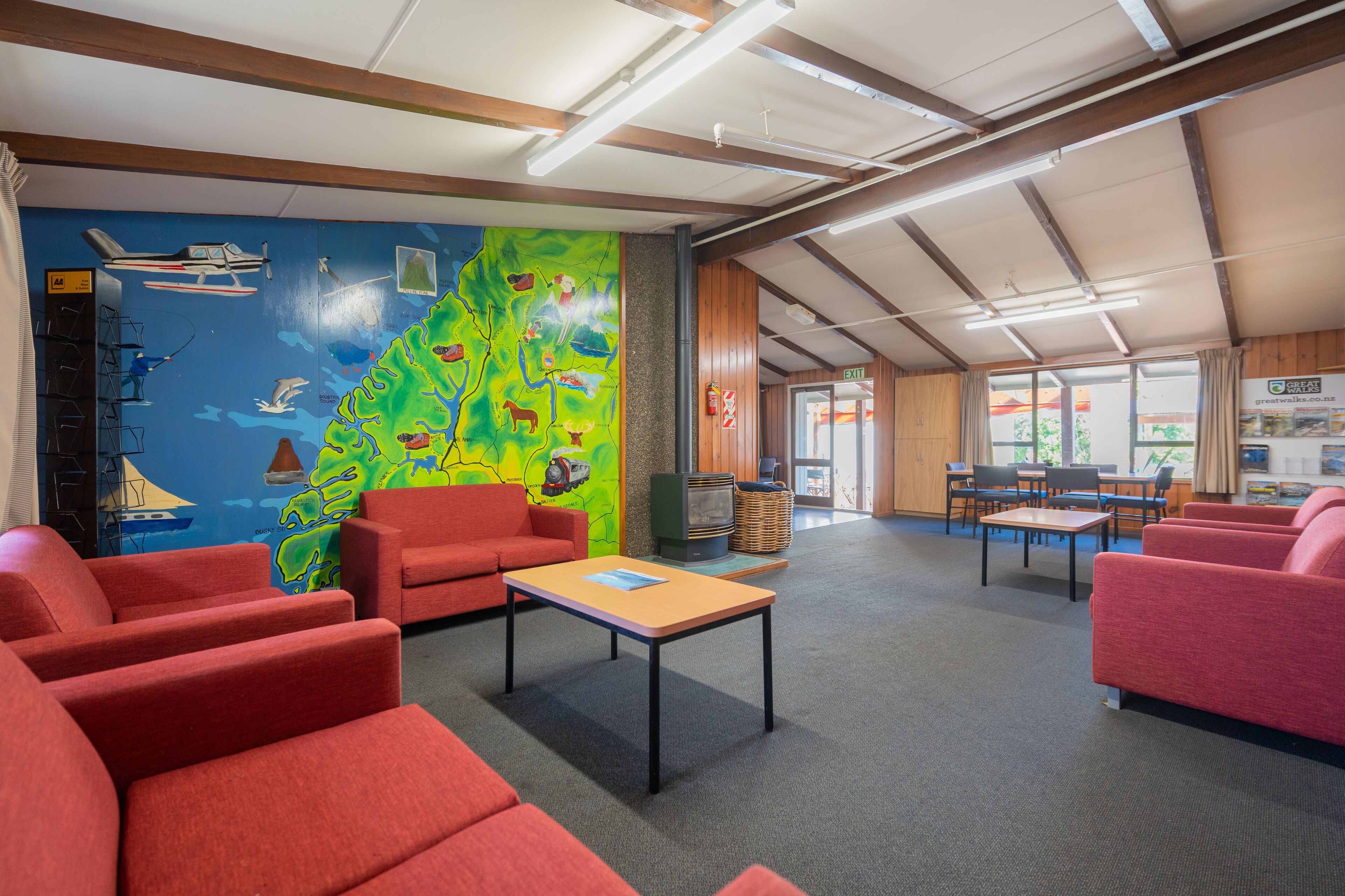 A spacious room with red sofas, a wooden table, and a colorful mural depicting a map and various animals.