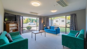 A living room with two green sofas, a coffee table, and a bookshelf. - Te Anau Central Backpackers (Te Anau)