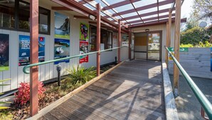 A covered walkway with wooden railings, posters advertising Milford Sound, and a clear view of the building's entrance. - Te Anau Central Backpackers (Te Anau)