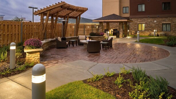 A courtyard with outdoor seating, a pergola, and a building with stone facade and windows. - Suite with Pool |  Business Essentials (Omaha)