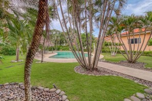 A pool surrounded by palm trees and a well-maintained lawn.