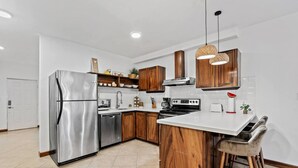Une cuisine moderne dotée d’un réfrigérateur en acier inoxydable, de meubles en bois, d’un îlot central avec des tabourets et d’un éclairage suspendu.