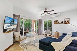 A modern living room with a television, seating, a ceiling fan, and a view of the outdoors.