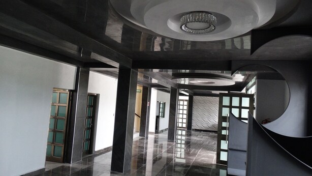 Un interior espacioso y moderno, con piso pulido, un elemento circular en el techo y vista a una escalera que lleva a otra zona.