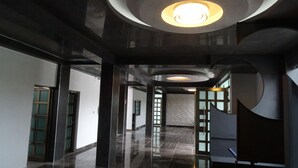 Un pasillo moderno con piso pulido, una lámpara circular y una puerta de vidrio que da a otra habitación.