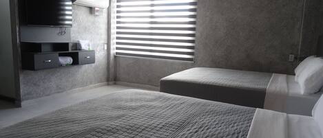 A bedroom with two beds, a built-in TV, and a window with blinds.