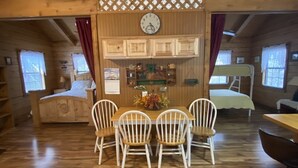 A cozy cabin interior with a wooden dining table, four chairs, a clock, and a decorative lattice panel. - A Peace of Heaven LOG Cabins & RV- Cabin #1 (Vanderpool)