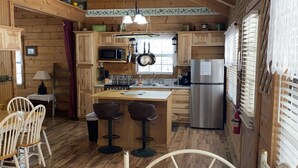 A cozy cabin-style kitchen with wooden walls, a central island with stools, a refrigerator, and a microwave. - A Peace of Heaven LOG Cabins & RV- Cabin #1 (Vanderpool)