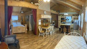 A cozy log cabin with a wooden interior, a dining area with white chairs, a kitchen with modern appliances, and a bed with a wooden headboard. - A Peace of Heaven LOG Cabins & RV- Cabin #1 (Vanderpool)