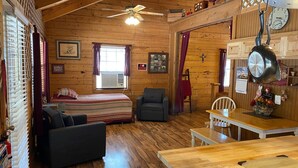 A cozy cabin with a bed, a sofa, a dining table, and a ceiling fan. - A Peace of Heaven LOG Cabins & RV- Cabin #3 (Vanderpool)