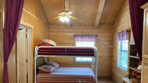 A wooden cabin room with a bunk bed, a ceiling fan, and a window with shutters. - A Peace of Heaven LOG Cabins & RV- Cabin #3 (Vanderpool)