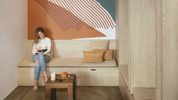 A cozy seating area with a mural, a wooden bench, and a small table with a croissant and sunglasses.