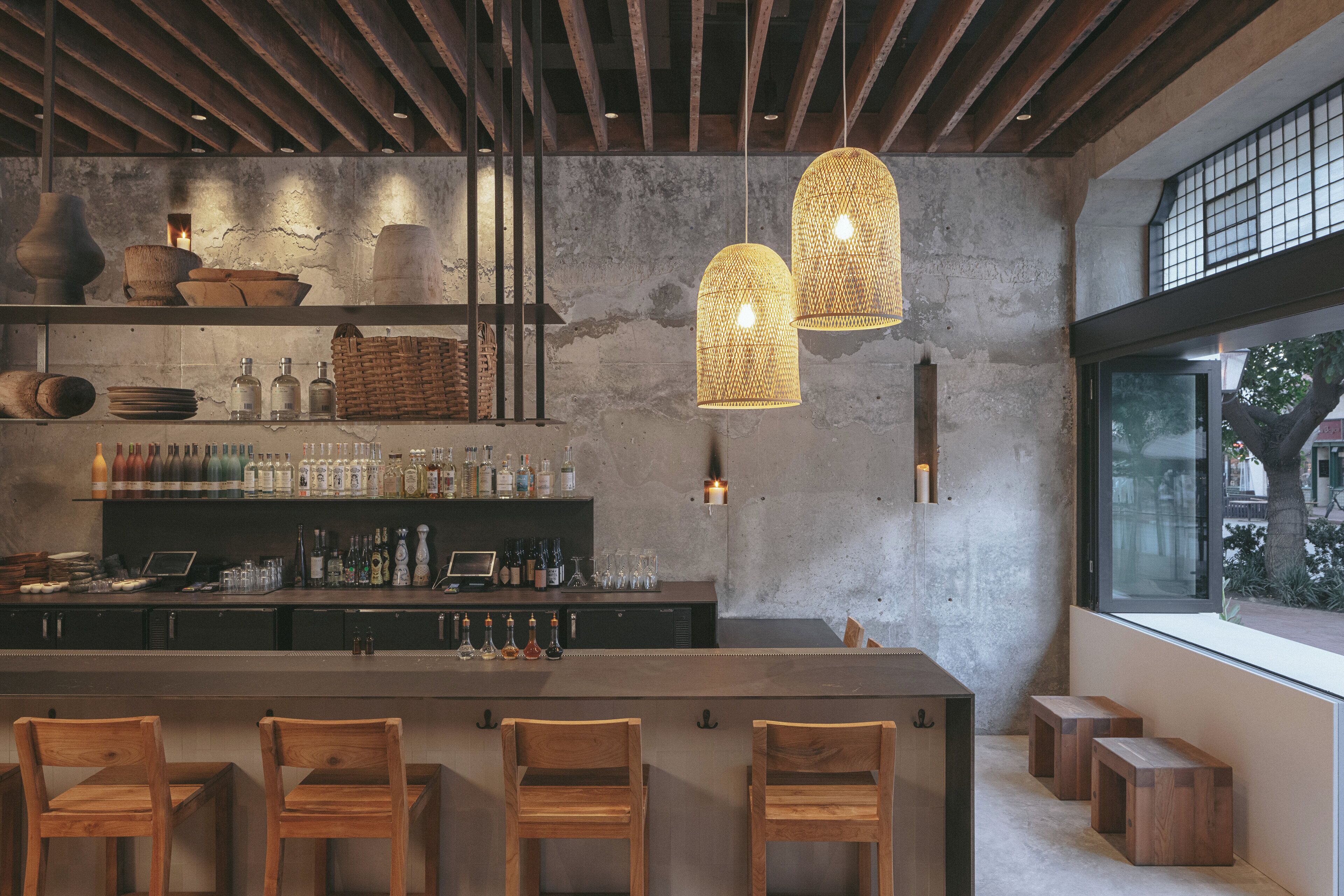 Un espace bar avec des chaises en bois, un comptoir, des étagères remplies de bouteilles et des luminaires suspendus.