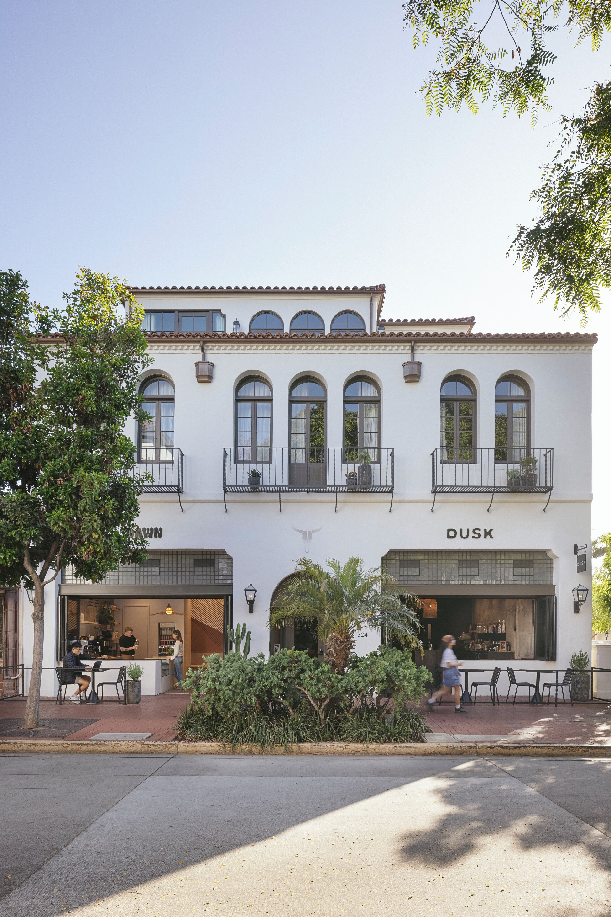 Un bâtiment blanc avec une enseigne indiquant « DUSK » au rez-de-chaussée, doté d’une terrasse et d’un petit jardin.
