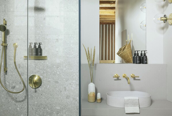 Un baño moderno con ducha envuelta en vidrio, un lavabo blanco con detalles dorados y un espejo sobre el lavabo.