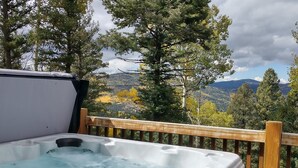 Un bain à remous sur une terrasse en bois, offrant une vue magnifique sur les arbres et les montagnes.