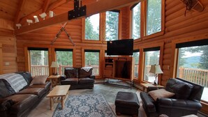 L’intérieur d’une cabane en rondins est aménagé avec un grand téléviseur, des meubles en cuir et de nombreuses fenêtres qui offrent une vue sur l’extérieur.