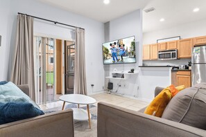 A modern living room with a flat-screen TV, a dining area, and a kitchen with wooden cabinets.