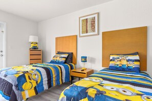 A bedroom with two beds, each with a Minion-themed duvet, a bedside table with a lamp, and a framed picture on the wall.