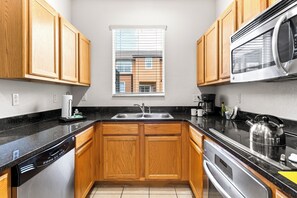 Una cocina moderna con armarios de madera, un lavamanos de acero inoxidable y un microondas integrado.