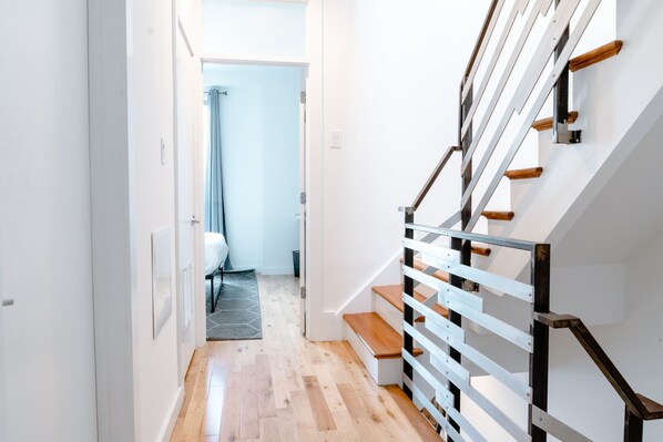 A modern staircase with wooden steps and metal railings, leading to a room with a light blue curtain and a gray carpet.