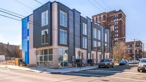 A modern multi-story building with large windows and a flat roof, located at a street corner with cars parked nearby. - Fantastic 4BR Townhouse W/ HOTTUB (Philadelphia)