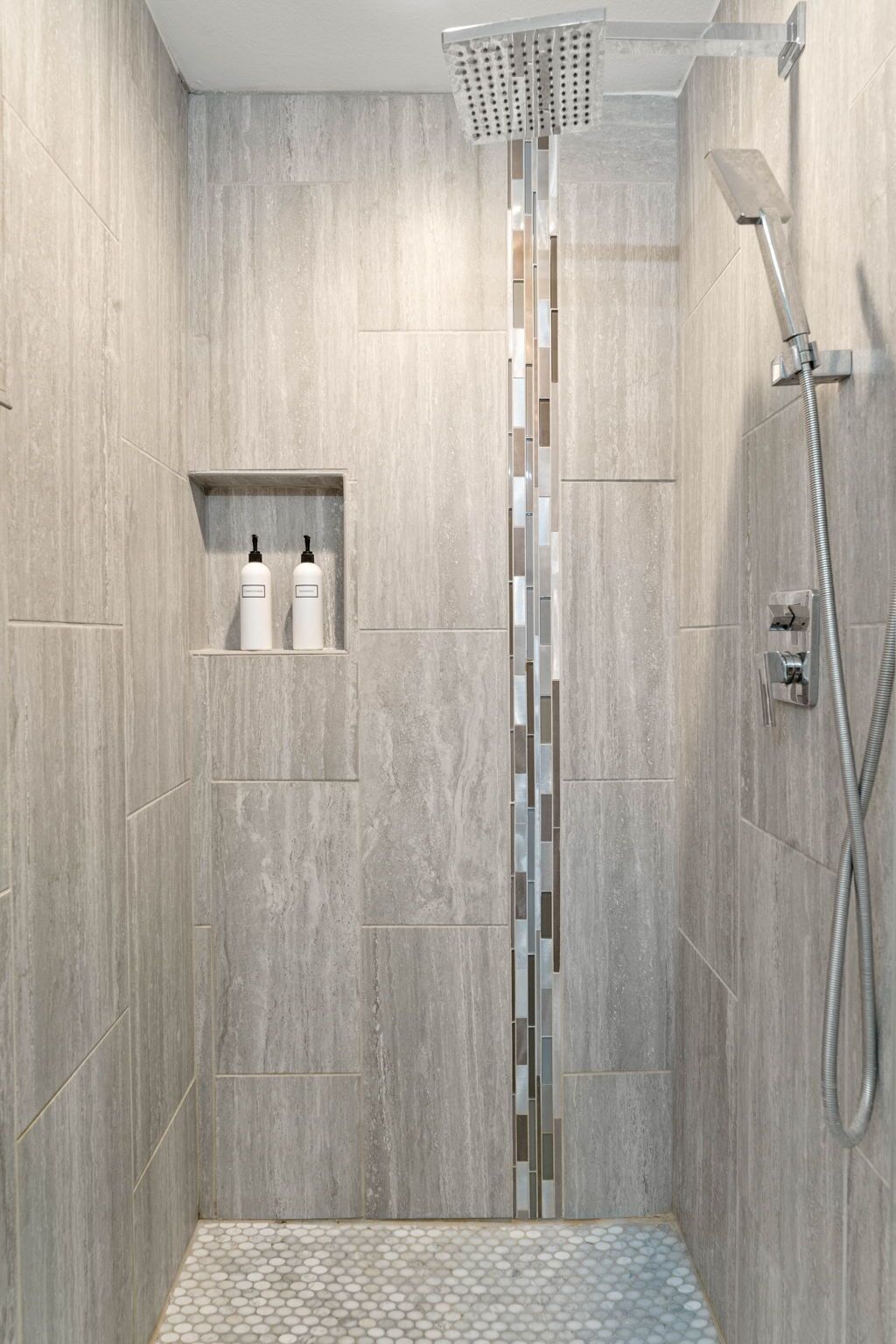A modern shower with a rain showerhead, a handheld showerhead, and a tiled floor.