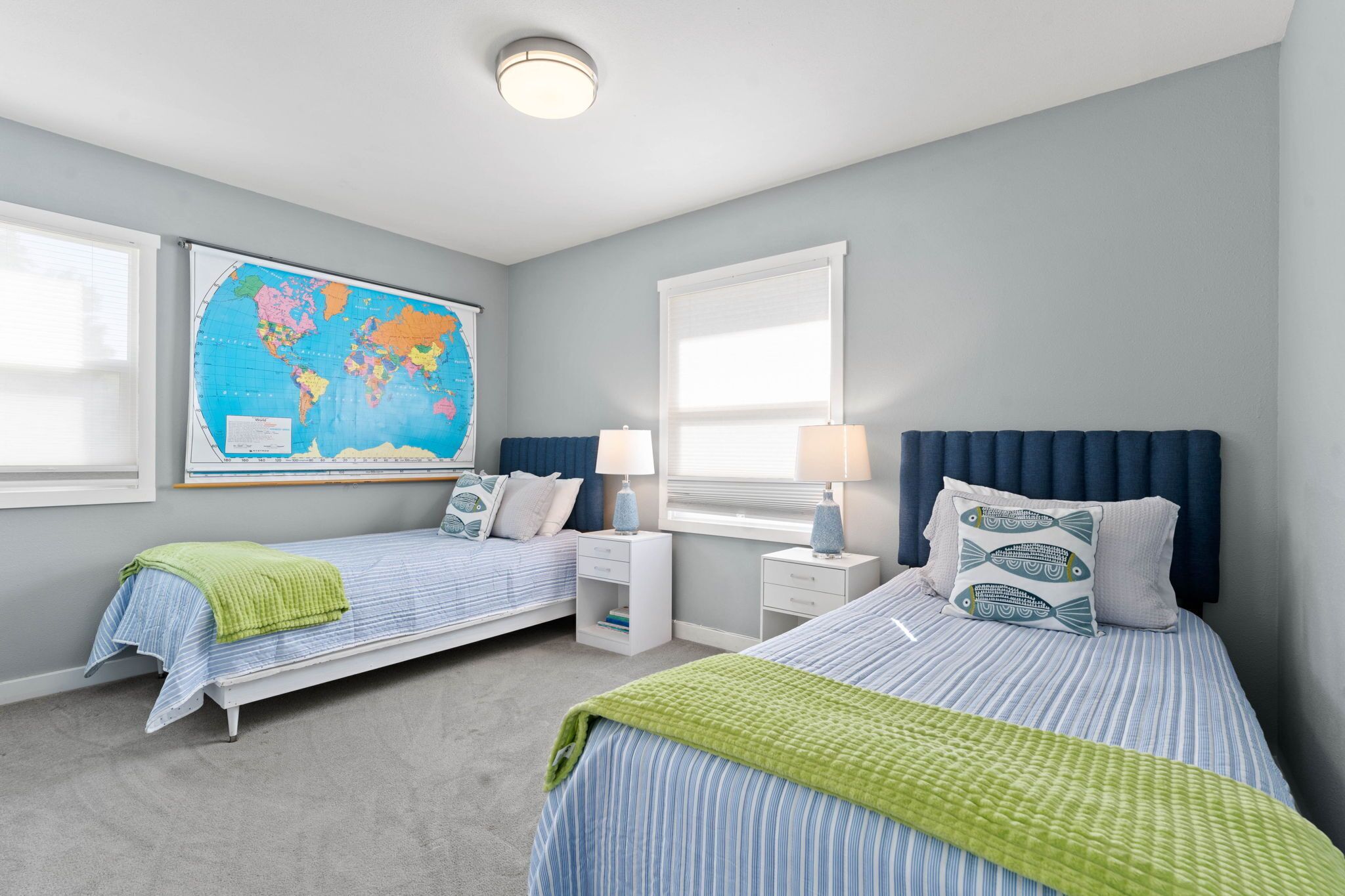Une chambre avec deux lits simples, une carte du monde accrochée au mur et une fenêtre avec des stores.