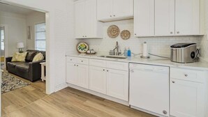 Una cocina moderna con muebles blancos, una cafetera de acero inoxidable y un lavavajillas.