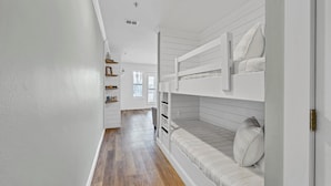 Un pasillo estrecho con suelo de madera, paredes blancas y literas a un lado.