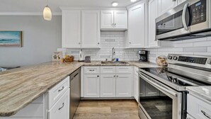 Cocina moderna con armarios blancos, encimera de granito, electrodomésticos de acero inoxidable y suelo de madera.