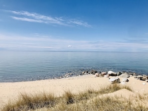 Une plage à l’eau claire, avec un rivage sablonneux et quelques rochers épars.