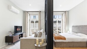 A modern hotel room with a bed, a sofa, a TV, and a small table with candles.