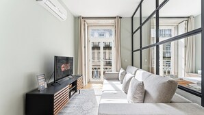 A modern living room with a sofa, a TV, and a window with a view of a balcony. - GuestReady - Modern Apartment in Bolhão (Porto)