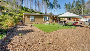 Een chalet met een overdekt terras, een kleine gazon en een bebost achtergrond.